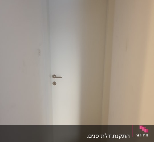 דלת לבנה עם ידית כסופה בקיר לבן